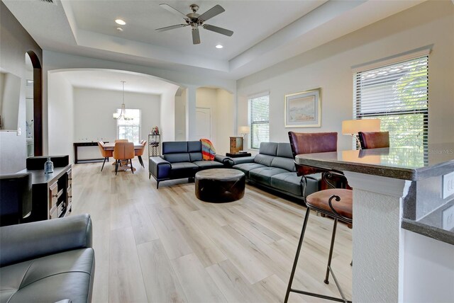 living room with ceiling fan, a tray ceiling, and light wood-type flooring
