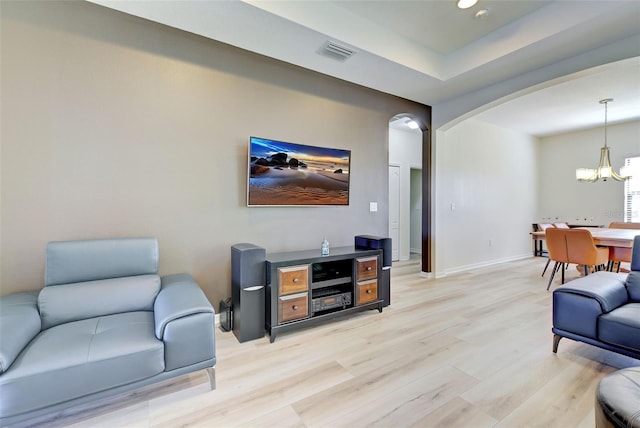 living room featuring a tray ceiling, light hardwood / wood-style flooring, and a chandelier