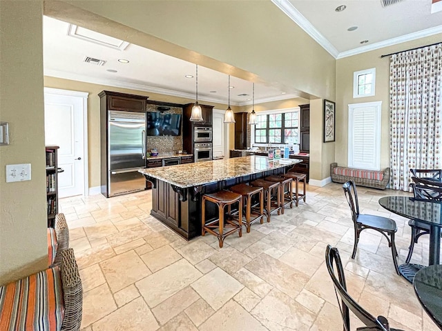 kitchen featuring pendant lighting, stainless steel appliances, a kitchen breakfast bar, light stone countertops, and a kitchen island