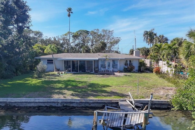 back of house with a sunroom, a water view, and a lawn