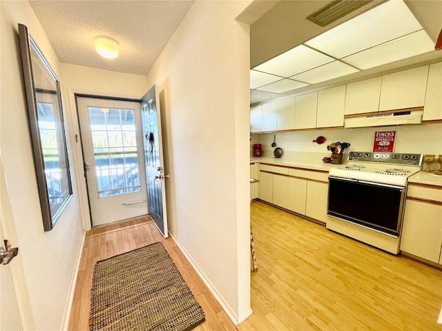 kitchen with electric range, light hardwood / wood-style flooring, range hood, a textured ceiling, and cream cabinetry