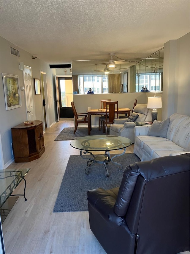 living room with ceiling fan, light hardwood / wood-style floors, and a textured ceiling