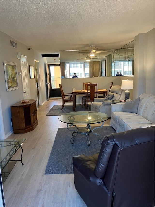 living room with light wood-type flooring, ceiling fan, and a textured ceiling