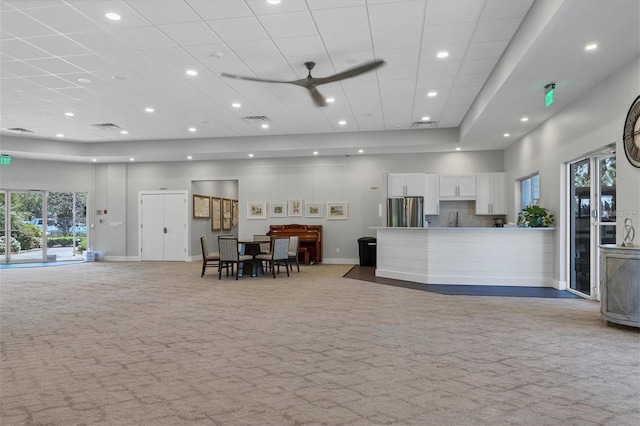 interior space featuring a towering ceiling, stainless steel refrigerator, white cabinetry, backsplash, and light colored carpet