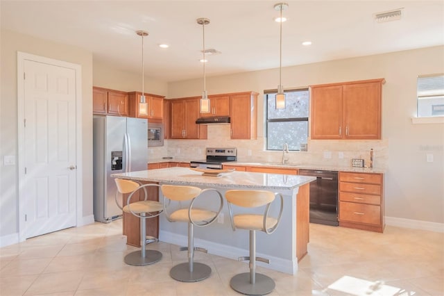 kitchen with light stone counters, stainless steel appliances, sink, pendant lighting, and a center island