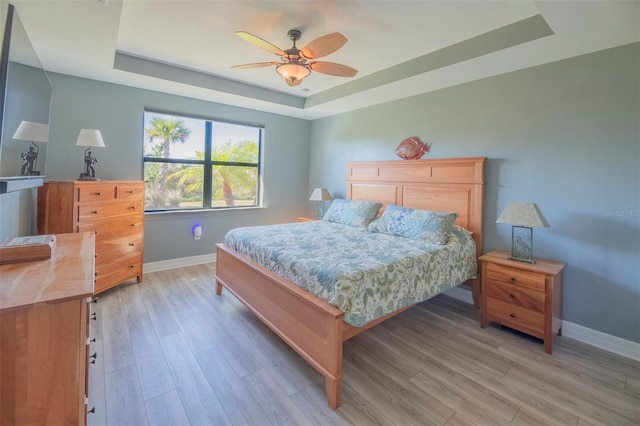 bedroom with ceiling fan, light wood-type flooring, and a tray ceiling