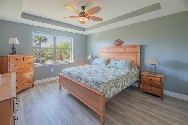 bedroom featuring ceiling fan, light hardwood / wood-style flooring, and a tray ceiling