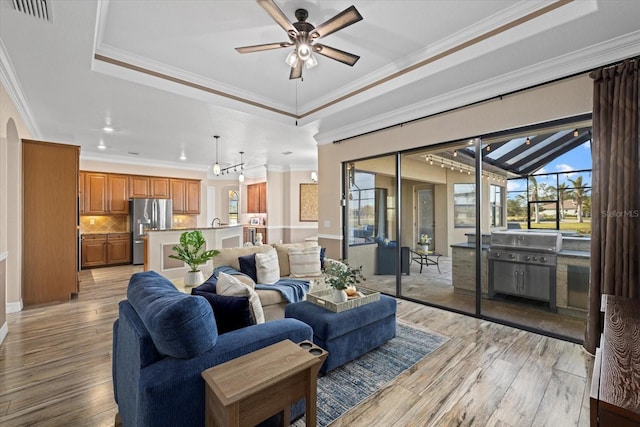 living room with light hardwood / wood-style floors, ceiling fan, a raised ceiling, ornamental molding, and sink