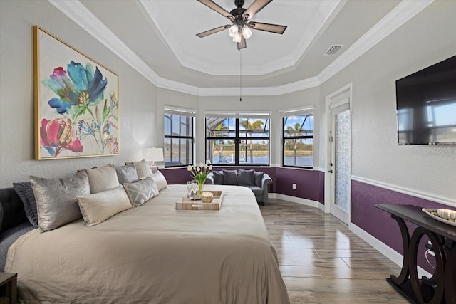 bedroom with ceiling fan, wood-type flooring, ornamental molding, and a raised ceiling