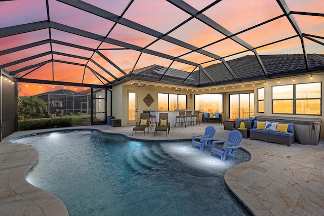 pool at dusk featuring glass enclosure, exterior bar, and a patio