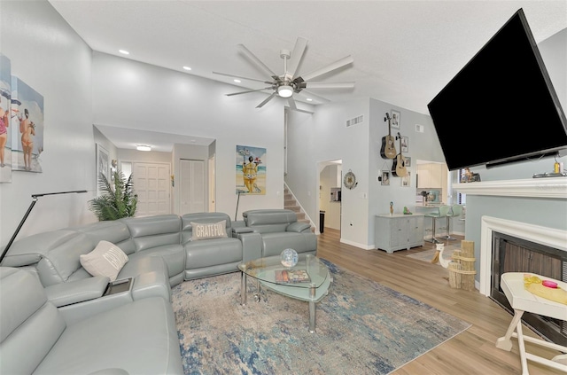 living room featuring a towering ceiling, light wood-type flooring, and ceiling fan