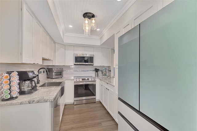 kitchen featuring white cabinetry, backsplash, light stone countertops, a tray ceiling, and appliances with stainless steel finishes