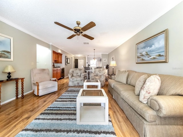 living room featuring ceiling fan, ornamental molding, a textured ceiling, and light hardwood / wood-style flooring