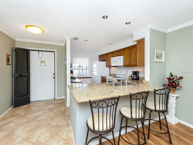 kitchen with white appliances, crown molding, light stone countertops, a textured ceiling, and kitchen peninsula