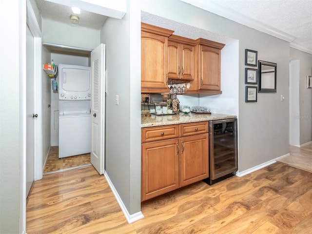 kitchen featuring light stone countertops, beverage cooler, stacked washer / dryer, light hardwood / wood-style floors, and a textured ceiling