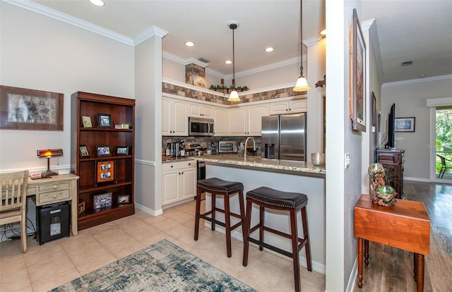 kitchen with white cabinetry, ornamental molding, stainless steel appliances, and a kitchen bar