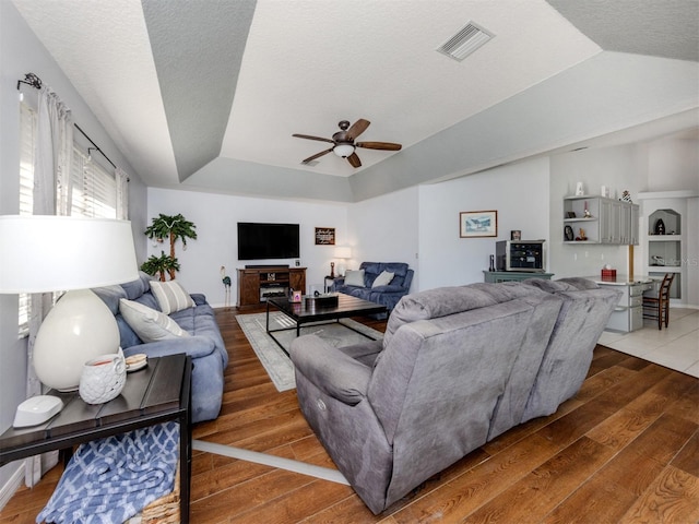 living room featuring hardwood / wood-style floors, ceiling fan, a fireplace, a textured ceiling, and a tray ceiling