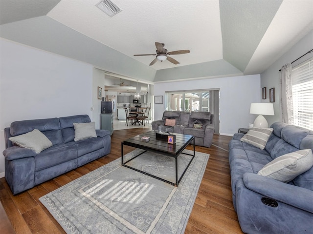 living room with a raised ceiling, lofted ceiling, ceiling fan, and dark hardwood / wood-style floors