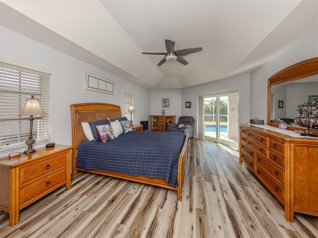 bedroom with access to exterior, ceiling fan, a raised ceiling, light hardwood / wood-style floors, and vaulted ceiling