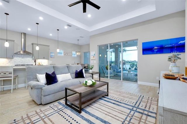 living room featuring ceiling fan, a raised ceiling, and light hardwood / wood-style flooring