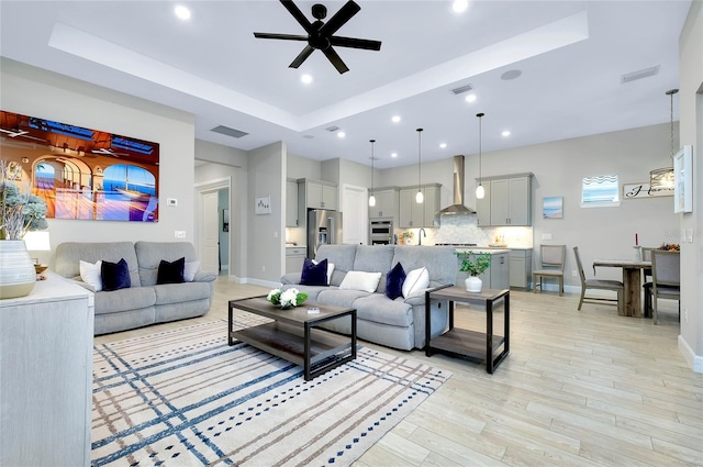 living room featuring light wood-type flooring, ceiling fan, and a raised ceiling