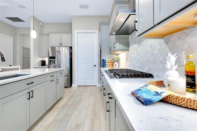 kitchen with backsplash, light hardwood / wood-style floors, sink, hanging light fixtures, and appliances with stainless steel finishes