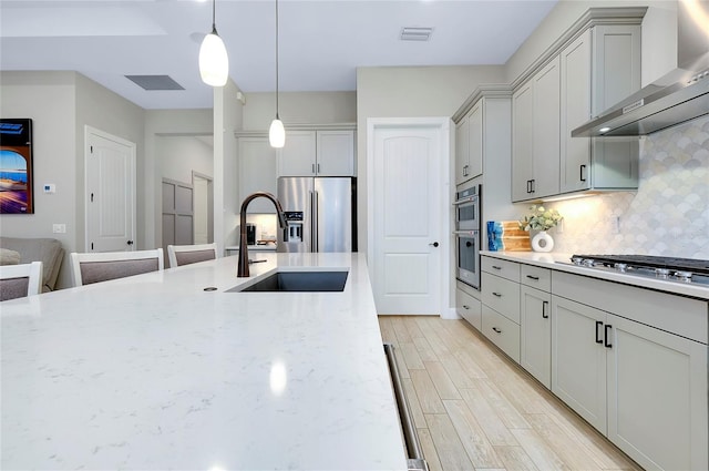 kitchen featuring light stone countertops, wall chimney range hood, stainless steel appliances, sink, and backsplash