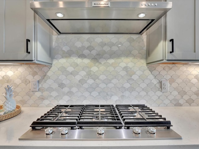 kitchen with stainless steel gas stovetop, exhaust hood, gray cabinetry, and backsplash