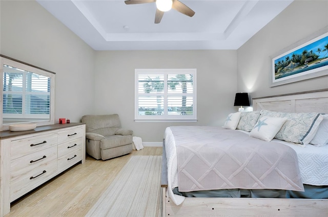 bedroom with ceiling fan, multiple windows, a tray ceiling, and light hardwood / wood-style flooring