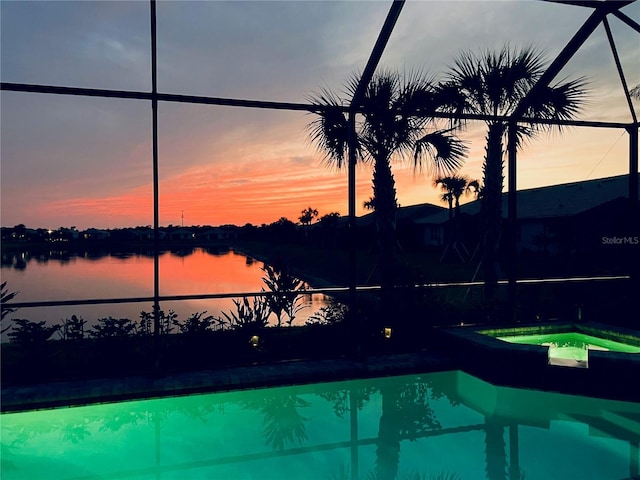 pool at dusk with an in ground hot tub, a lanai, and a water view