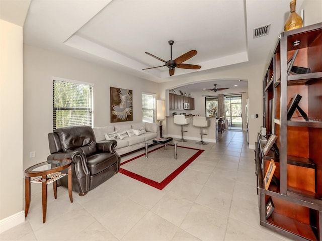 tiled living room featuring ceiling fan, a wealth of natural light, and a tray ceiling