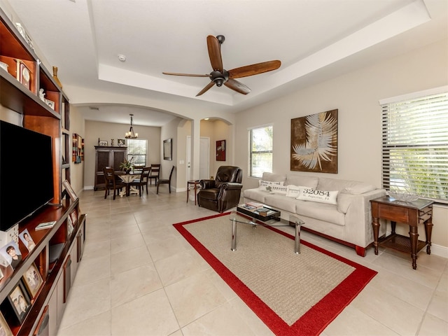 living room featuring ceiling fan with notable chandelier, light tile patterned flooring, and a tray ceiling