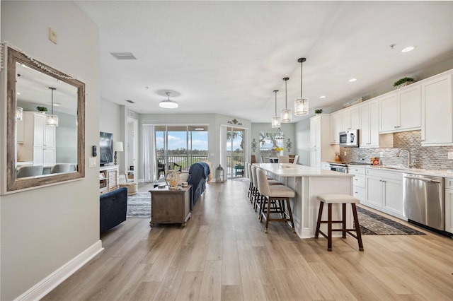 kitchen featuring appliances with stainless steel finishes, decorative light fixtures, white cabinetry, decorative backsplash, and a center island