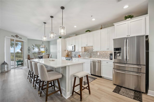 kitchen with appliances with stainless steel finishes, decorative light fixtures, white cabinetry, sink, and a center island