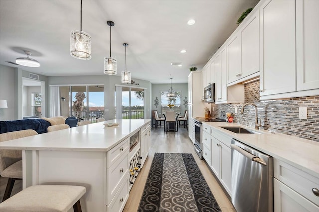 kitchen featuring sink, white cabinetry, hanging light fixtures, stainless steel appliances, and a kitchen bar