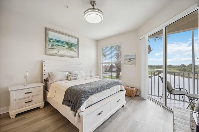 bedroom featuring a water view, light hardwood / wood-style flooring, and access to outside