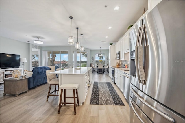 kitchen featuring white cabinetry, hanging light fixtures, a kitchen island, and appliances with stainless steel finishes