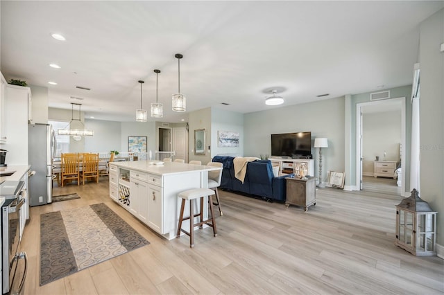 kitchen with a breakfast bar, appliances with stainless steel finishes, pendant lighting, a kitchen island with sink, and white cabinets