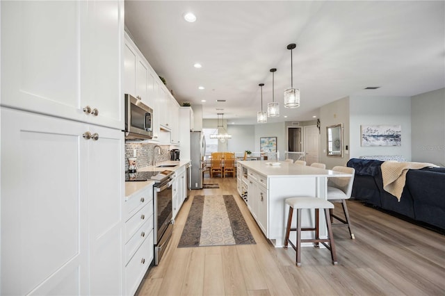 kitchen featuring pendant lighting, white cabinetry, a kitchen island, stainless steel appliances, and a kitchen bar