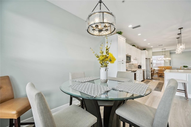 dining area featuring sink, a chandelier, and light hardwood / wood-style flooring