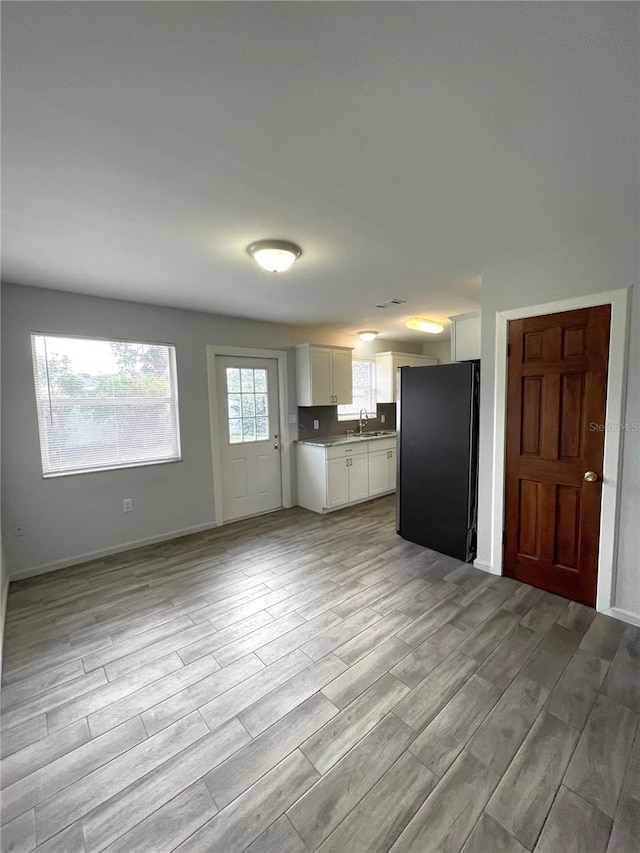 kitchen featuring white cabinets, light hardwood / wood-style floors, black fridge, and sink