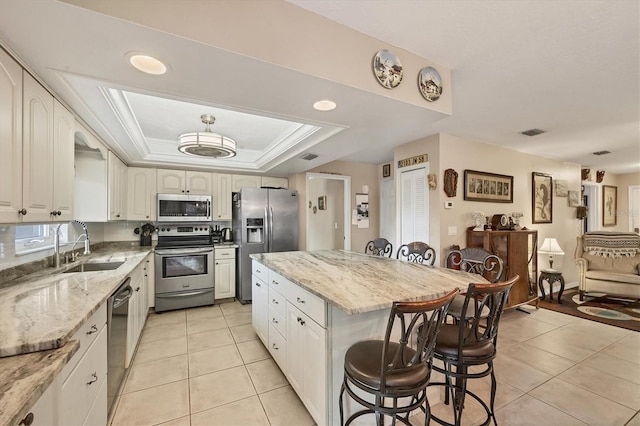 kitchen featuring light stone countertops, appliances with stainless steel finishes, a center island, sink, and a tray ceiling