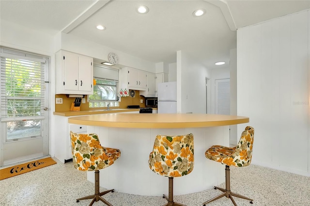 kitchen with white cabinetry, sink, a kitchen bar, white refrigerator, and kitchen peninsula