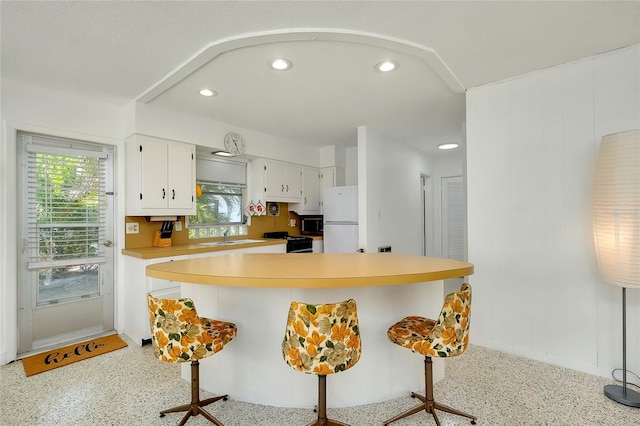 kitchen featuring a kitchen bar, sink, black gas range oven, white refrigerator, and white cabinets