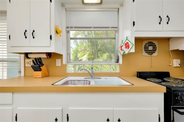 kitchen featuring plenty of natural light, black range with electric stovetop, sink, and white cabinets