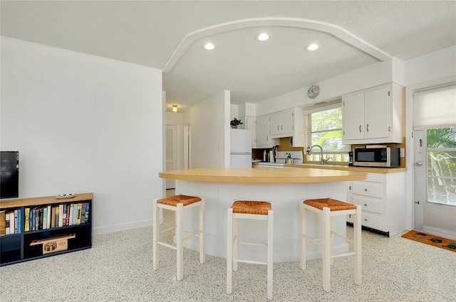 kitchen featuring white cabinetry, a kitchen bar, white refrigerator, and electric stove