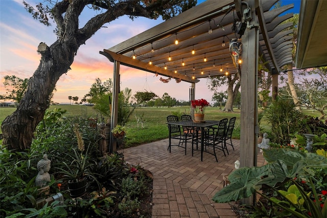 patio terrace at dusk featuring a pergola and a lawn