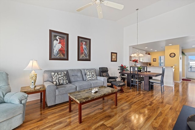 living room with wood-type flooring, ceiling fan with notable chandelier, and vaulted ceiling