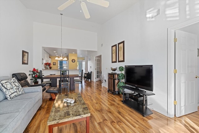 living room with a towering ceiling, ceiling fan with notable chandelier, and hardwood / wood-style flooring