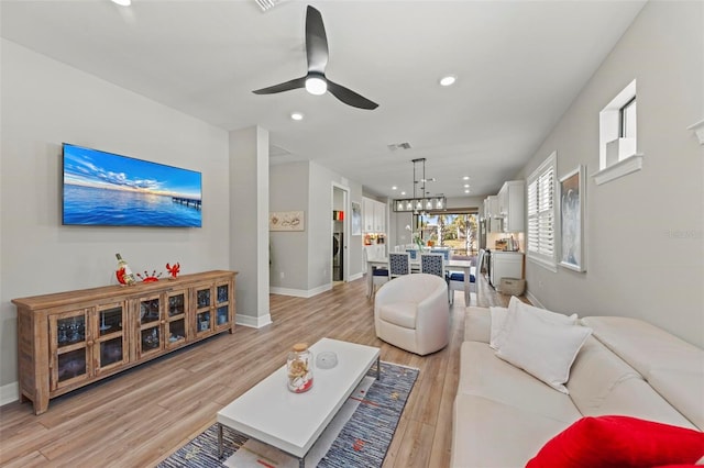 living room featuring ceiling fan with notable chandelier and light hardwood / wood-style floors